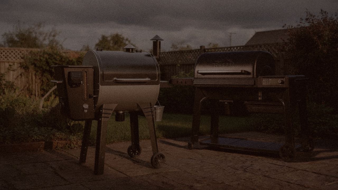 Camp Chef Woodwind WiFi 24 and Traeger Woodridge Pro at night with smoke, wood pellet grills on a dark patio