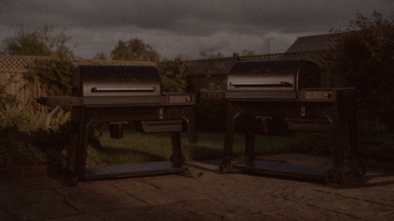 Traeger Timberline and Traeger Woodridge Pro at night with smoke, wood pellet grills on a dark patio